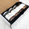 A white box filled with jars of Black Bow Sweets candied California cinnamon and sugar coated pecans, candied California cinnamon and sugar coated walnuts, candied rosemary truffle coated almonds, and sea salt and cracked black pepper toasted cashews.