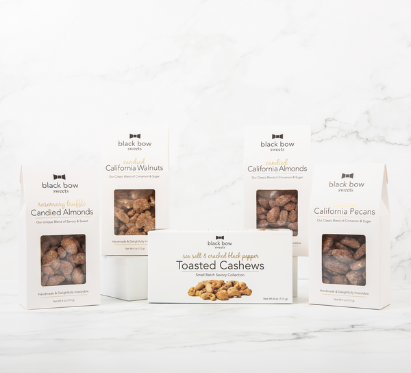 Packages of Black Bow Sweets candied California cinnamon and sugar pecans, candied rosemary truffle almonds, candied California cinnamon and sugar walnuts, candied California cinnamon and sugar almonds, and sea salt and cracked black pepper toasted cashews.
