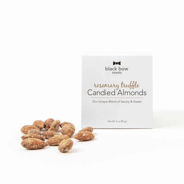 A Black Bow Sweets mini gift box of candied rosemary truffle almonds next to a small pile of almonds.