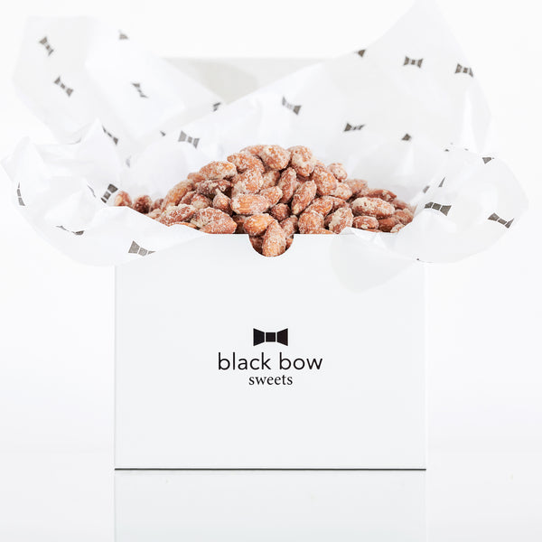 A white Black Bow Sweets gift box filled with candied rosemary truffle coated almonds loosely wrapped in white tissue paper with small black bows.
