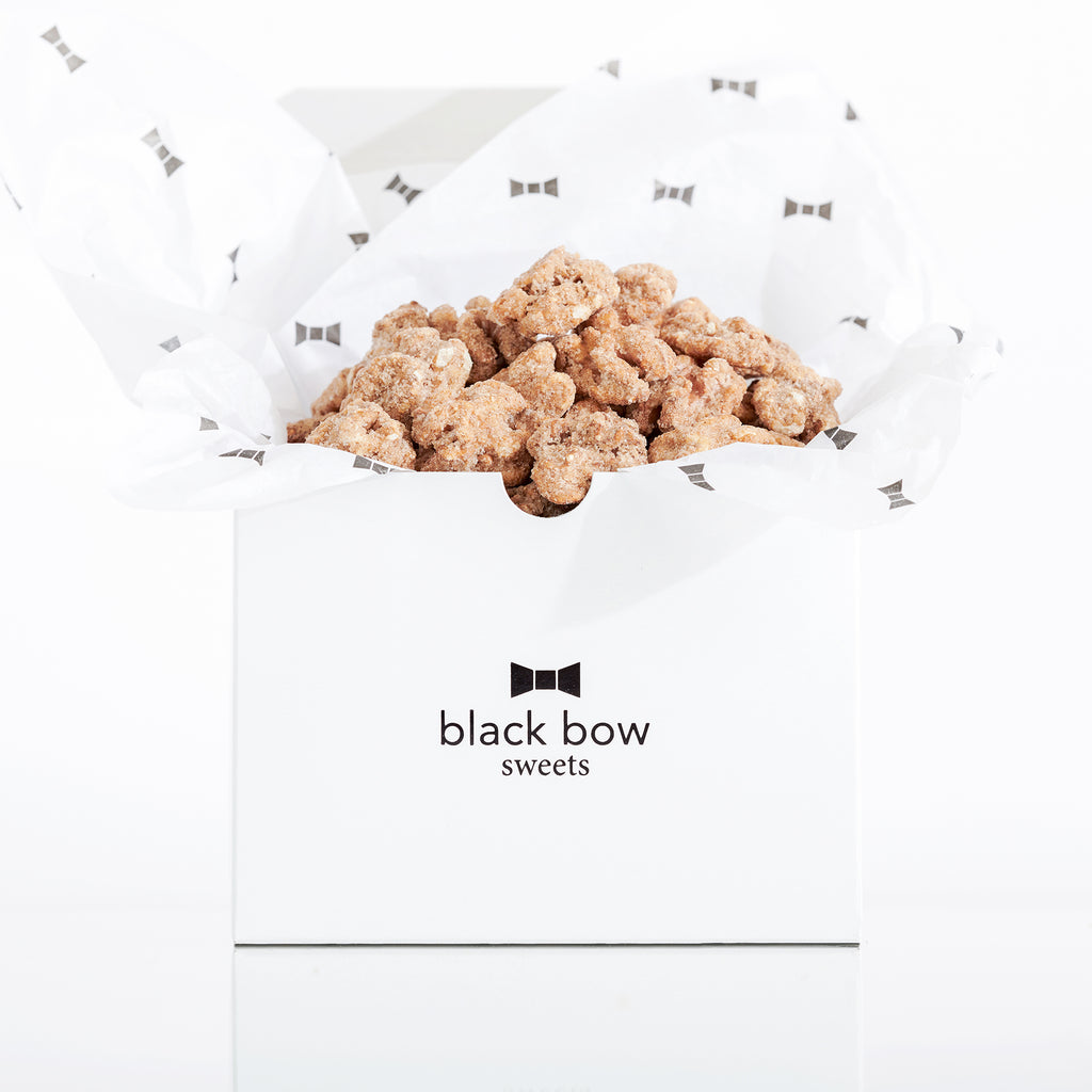 A white Black Bow Sweets gift box filled with candied California cinnamon and sugar coated walnuts loosely wrapped in white tissue paper with small black bows.