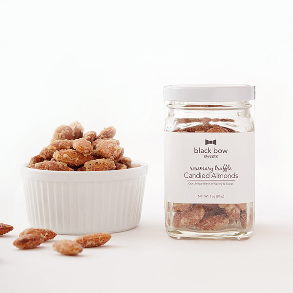 A jar of Black Bow Sweets candied rosemary truffle coated almonds next to a white bowl filled with the almonds.
