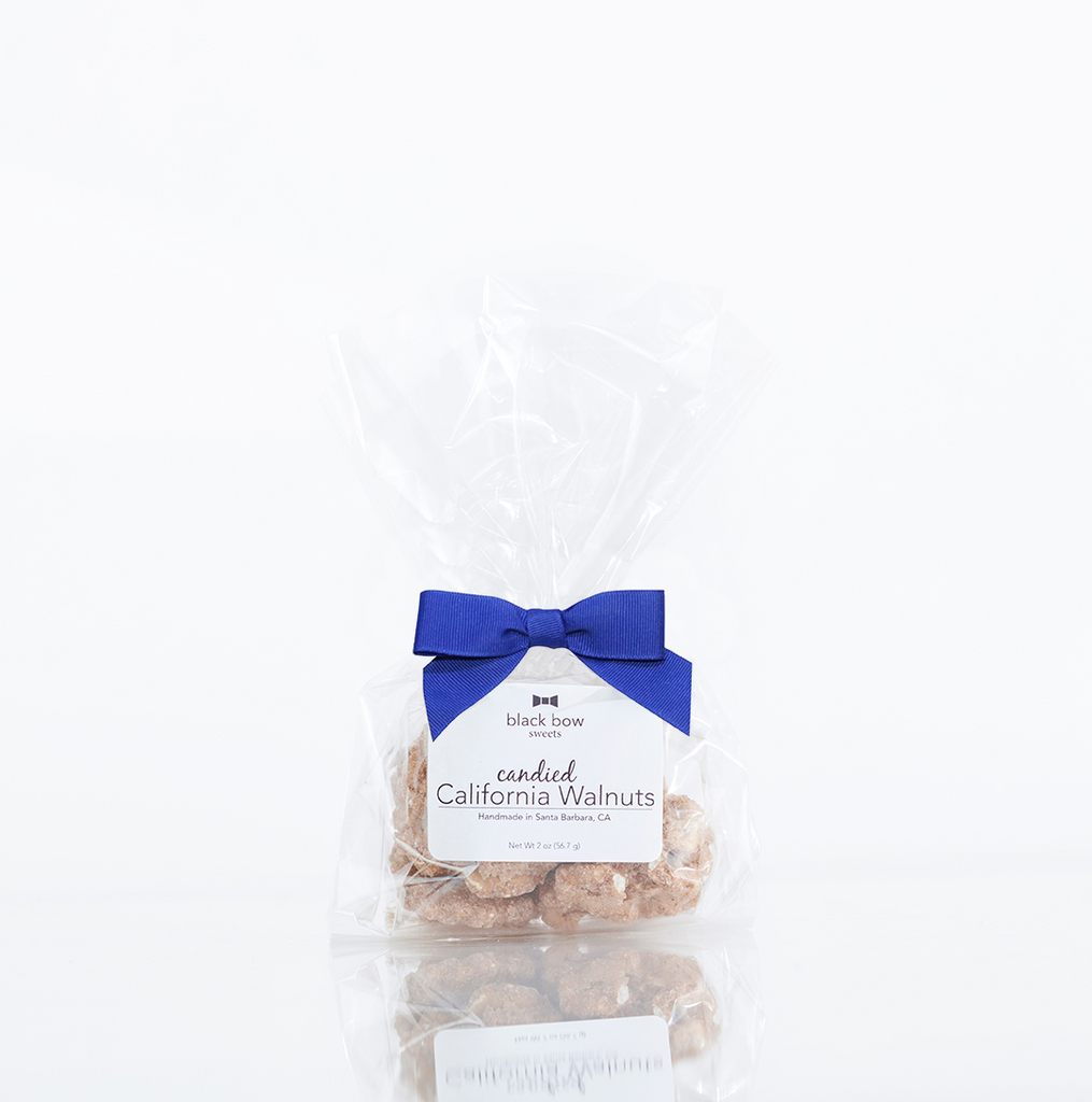 A bag of Black Bow Sweets candied California cinnamon and sugar coated pecans tied with a royal blue bow.