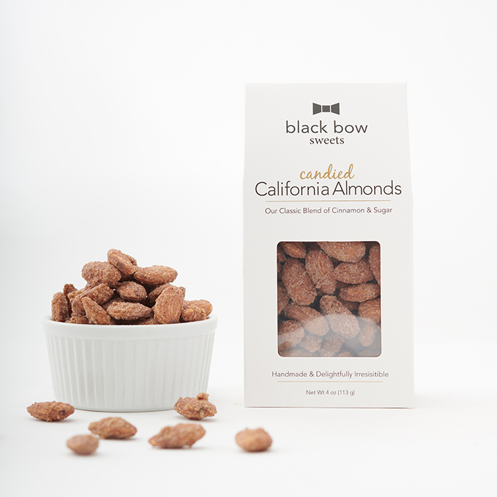 A box of Black Bow Sweets candied California cinnamon and sugar coated almonds next to a white bowl filled with the almonds.