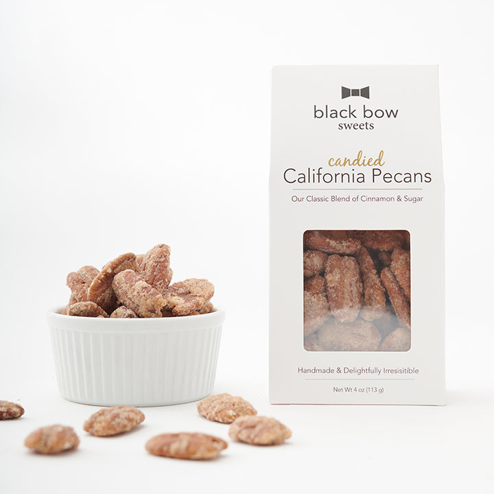 A box of Black Bow Sweets candied California cinnamon and sugar coated pecans next to a white bowl filled with the pecans.
