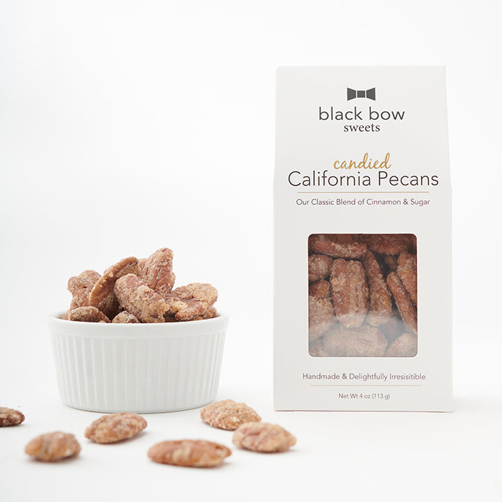 A package of Black Bow Sweets candied California cinnamon and sugar pecans next to a white bowl filled with the pecans.