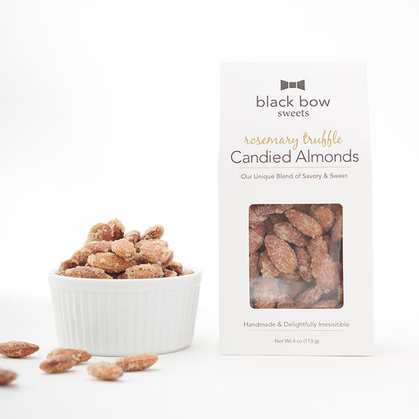 A box of Black Bow Sweets candied rosemary truffle coated almonds next to a white bowl filled with the almonds.
