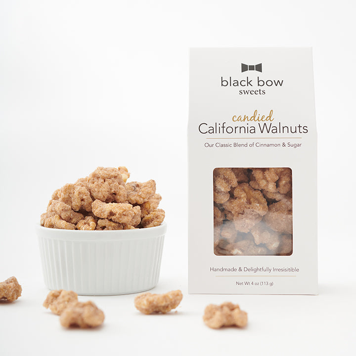 A package of Black Bow Sweets' candied California cinnamon and sugar coated walnuts next to a white bowl filled with the walnuts.