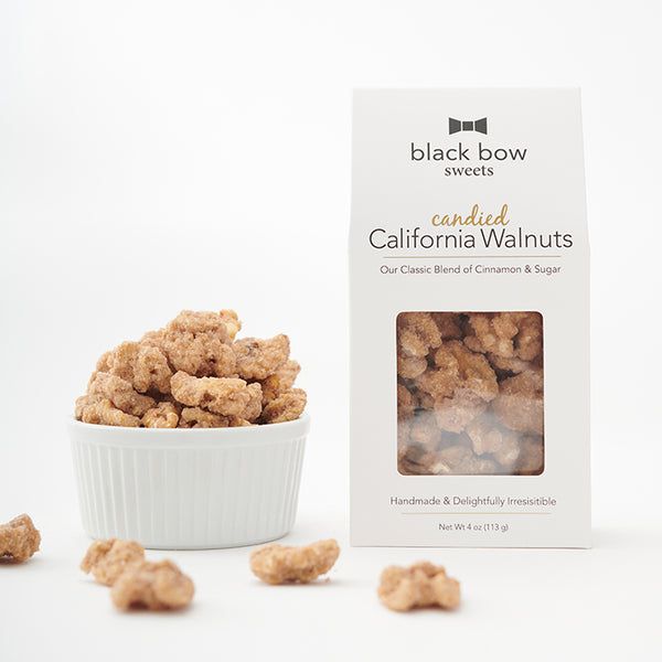 A box of Black Bow Sweets candied California cinnamon and sugar coated walnuts next to a white bowl filled with the walnuts.